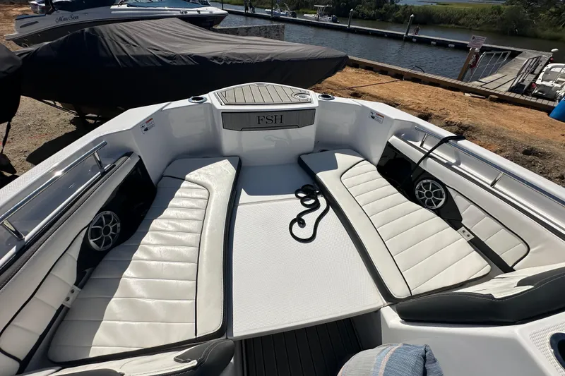 Slide: The Image of 2023 Yamaha Boats 252 FSH Sport interior with white seating and speakers, dockside view. - 28
