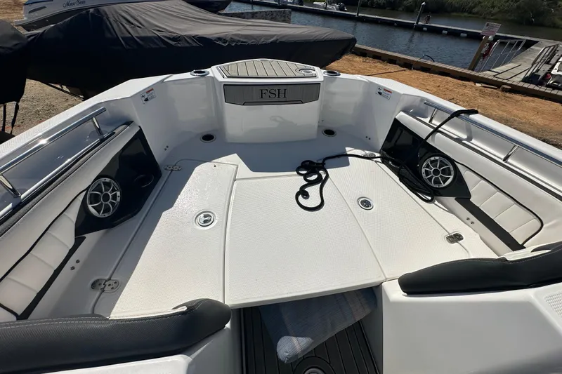 Slide: The Image of 2023 Yamaha Boats 252 FSH Sport interior with speakers and seating, docked by the water. - 31