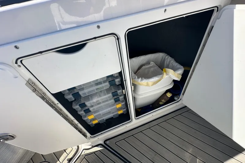 Slide: The Image of Storage compartment on 2023 Yamaha Boats 252 FSH Sport, featuring organized tackle boxes and trash bin. - 32