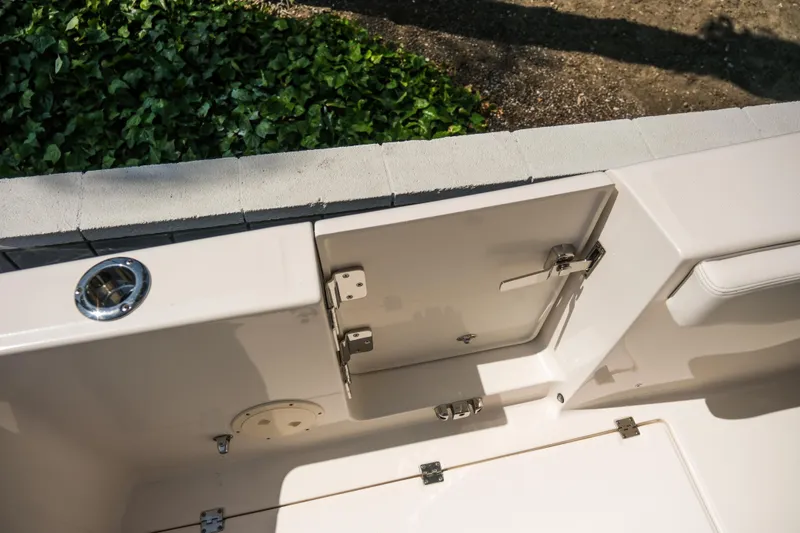 Slide: The Image of 2023 Robalo R302 Center Console boat interior detail with storage compartment and lush greenery background. - 25