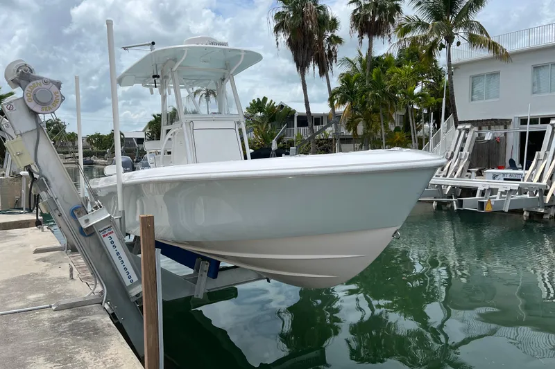 The Image of 2015 Contender 24 Sport boat on lift, dockside with palm trees and cloudy sky. - 1