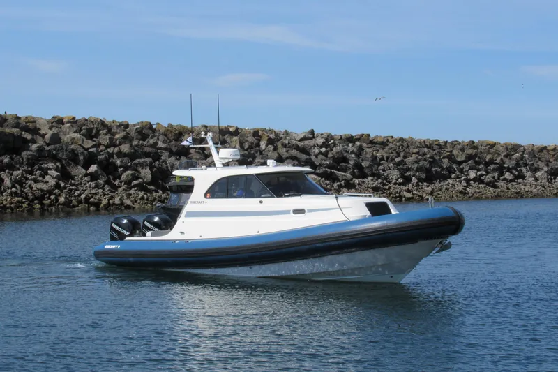Slide: The Image of 2017 Ribcraft Express 32 boat cruising near rocky shoreline under clear sky. - 4