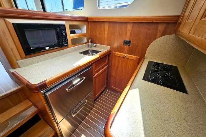 Slide: The Image of 2007 Mainship 34 Trawler kitchen with microwave, sink, stove, and wooden cabinetry. - 13