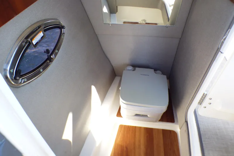 Slide: The Image of 2018 Chaparral 267 SSX boat interior with compact marine toilet and porthole window. - 21