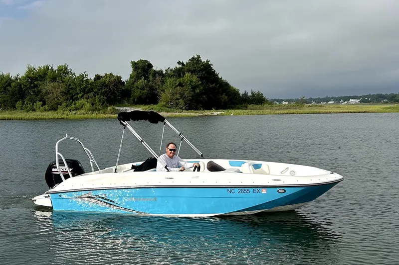 Slide: The Image of 2022 Bayliner Element E18 boat cruising on a calm lake with lush greenery. - 0