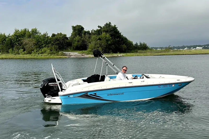 Slide: The Image of 2022 Bayliner Element E18 boat cruising on a calm lake with lush greenery. - 1