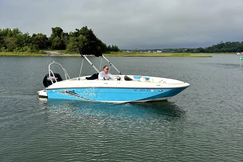 Slide: The Image of 2022 Bayliner Element E18 boat cruising on a calm lake with lush greenery. - 2