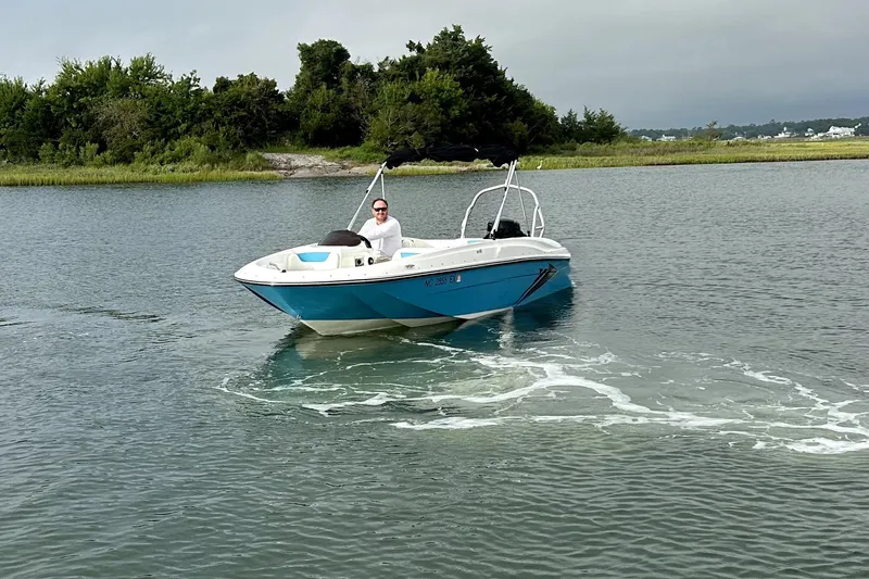 Slide: The Image of 2022 Bayliner Element E18 boat cruising on a calm lake with lush greenery. - 38