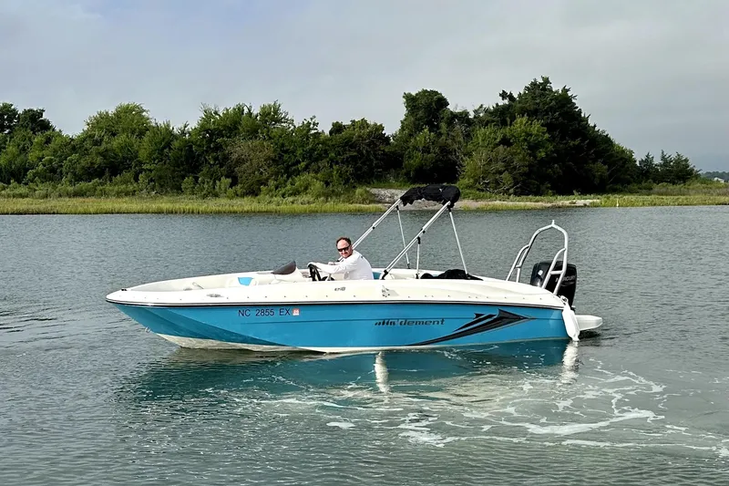 Slide: The Image of 2022 Bayliner Element E18 boat cruising on a calm lake with lush greenery. - 7