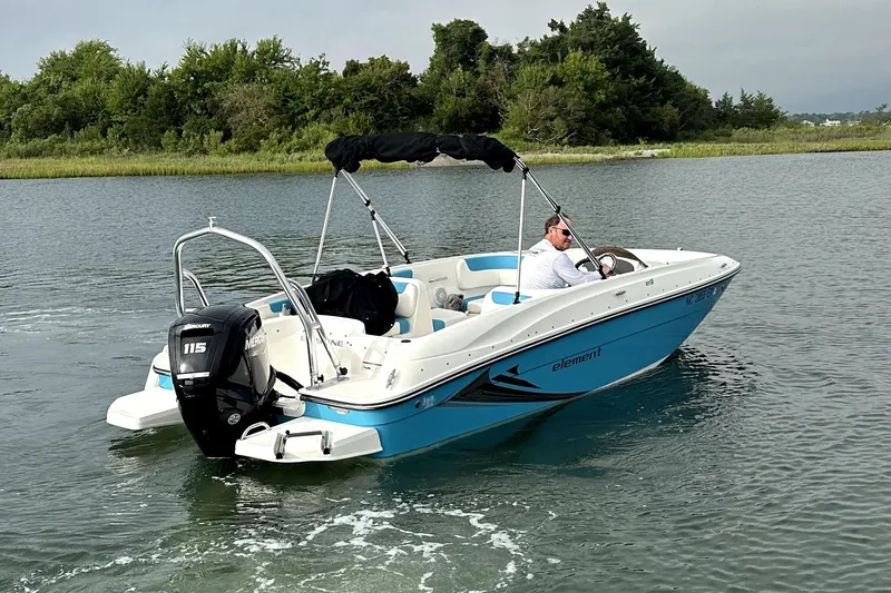 Slide: The Image of 2022 Bayliner Element E18 boat cruising on a calm lake with lush greenery. - 8