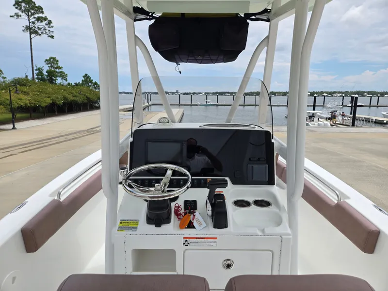 Slide: The Image of 2019 Sea Hunt 225 Ultra boat dashboard with steering wheel and controls, docked by the water. - 5