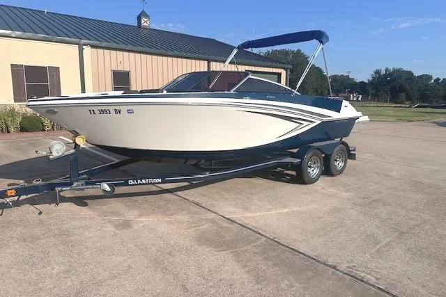 Slide: The Image of 2017 Glastron GT 205 boat on trailer, parked outdoors near a building. - 0