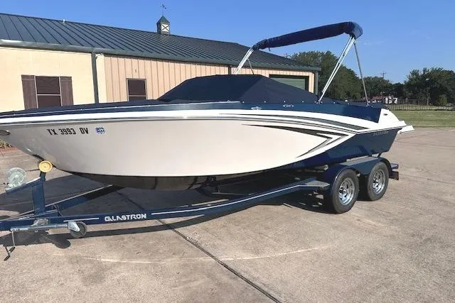 Slide: The Image of 2017 Glastron GT 205 boat on trailer, parked outdoors with a building in the background. - 29