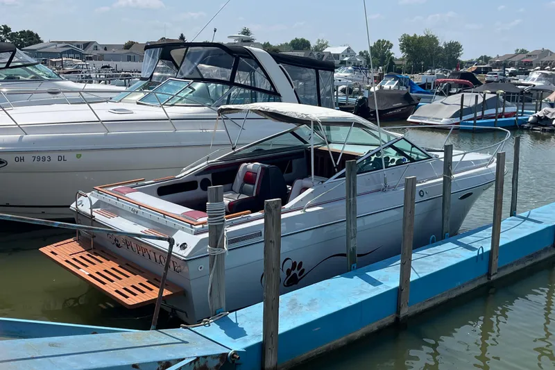 Slide: The Image of 1988 Four Winns 235 Sundowner boat docked at a marina, surrounded by other vessels. - 2