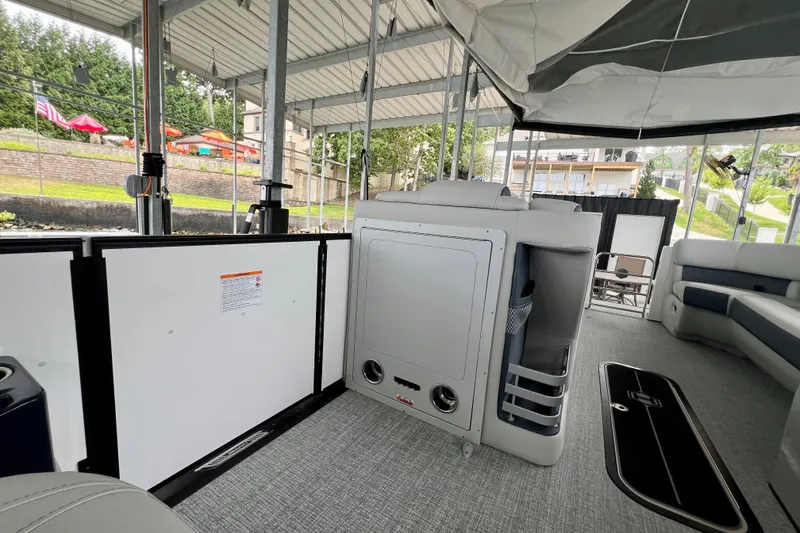 Slide: The Image of 2025 Harris Grand Mariner 250 interior with seating and storage, docked under a covered area. - 13