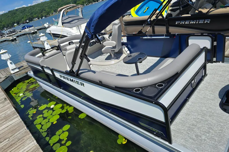 Slide: The Image of 2025 Premier 230 Sunsation RE pontoon boat docked by a scenic lake. - 3