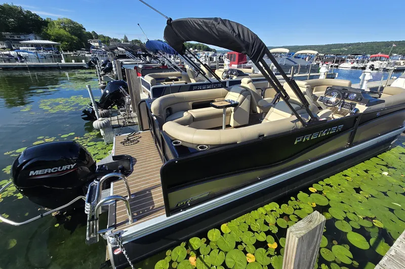 Slide: The Image of 2025 Premier 230 SunSation RF pontoon boat docked, featuring Mercury engine, surrounded by lily pads. - 2