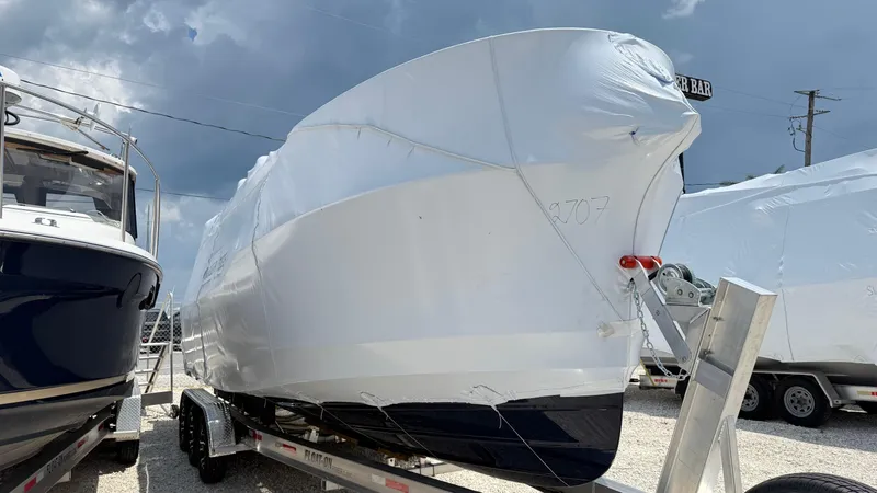 The Image of 2026 Ranger Tugs R-27 boat covered in protective wrap on a trailer under cloudy skies. - 0
