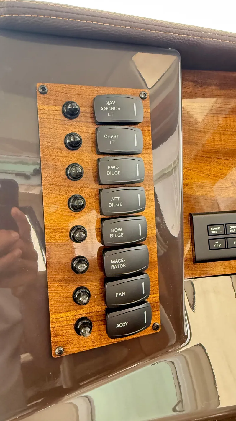 Slide: The Image of Control panel of 2026 Ranger Tugs R-27 boat with labeled switches on wood finish. - 18