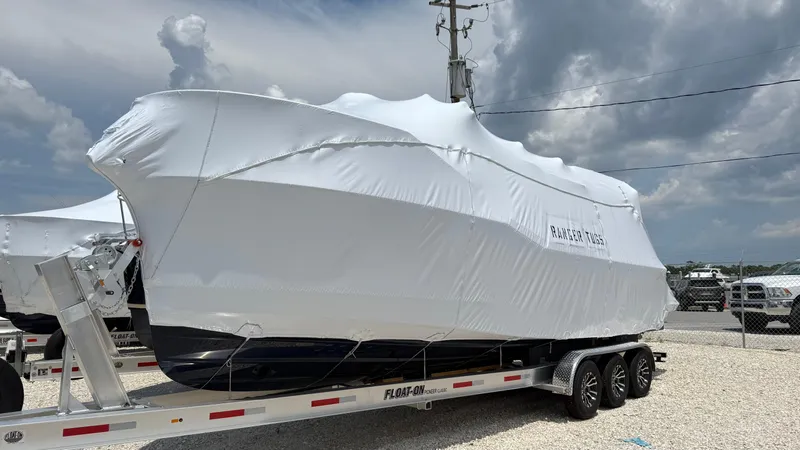 Slide: The Image of 2026 Ranger Tugs R-27 boat covered on trailer under cloudy sky. - 2