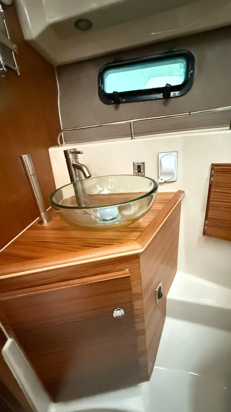 Slide: The Image of 2026 Ranger Tugs R-27 bathroom with glass sink and wooden cabinetry. - 45