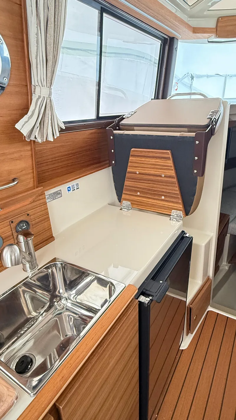 Slide: The Image of 2026 Ranger Tugs R-27 interior kitchen with sink, wooden cabinetry, and window view. - 39