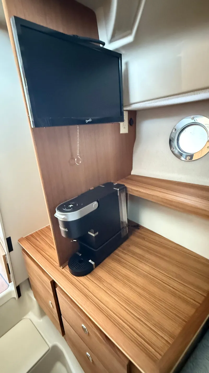 Slide: The Image of 2026 Ranger Tugs R-27 interior with TV and coffee maker on wooden counter. - 42