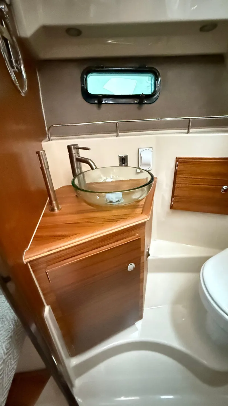 Slide: The Image of 2026 Ranger Tugs R-27 bathroom with glass sink, wooden cabinetry, and small window. - 47
