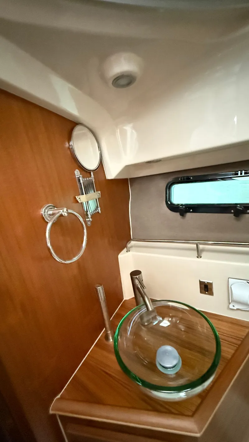 Slide: The Image of 2026 Ranger Tugs R-27 bathroom with glass sink, wooden countertop, and porthole window. - 49