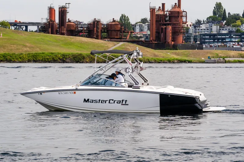 Slide: The Image of 2008 MasterCraft MariStar 235 SS boat cruising on a lake near industrial structures. - 2