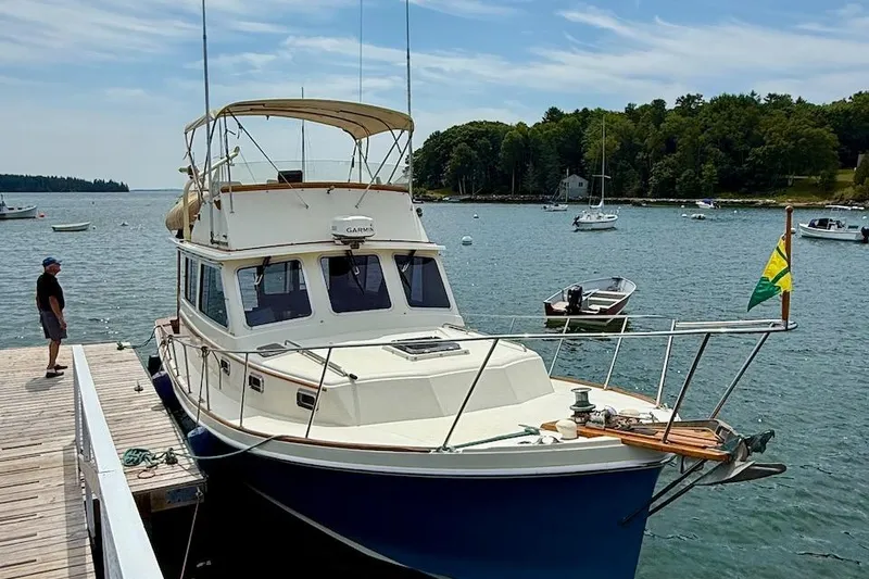 Slide: The Image of 1990 Nauset Flybridge Cruiser with extended hardtop docked in a scenic harbor. - 2