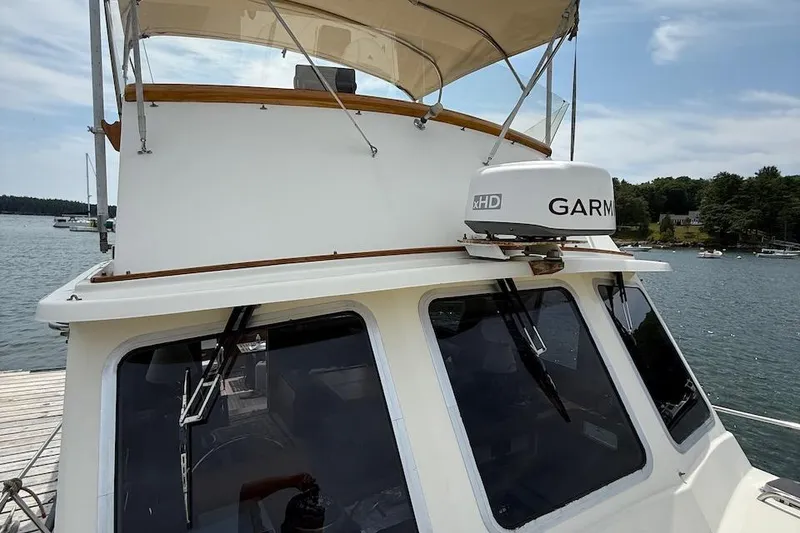 Slide: The Image of 1990 Nauset Flybridge Cruiser with extended hardtop, featuring Garmin radar, docked by a scenic lake. - 36