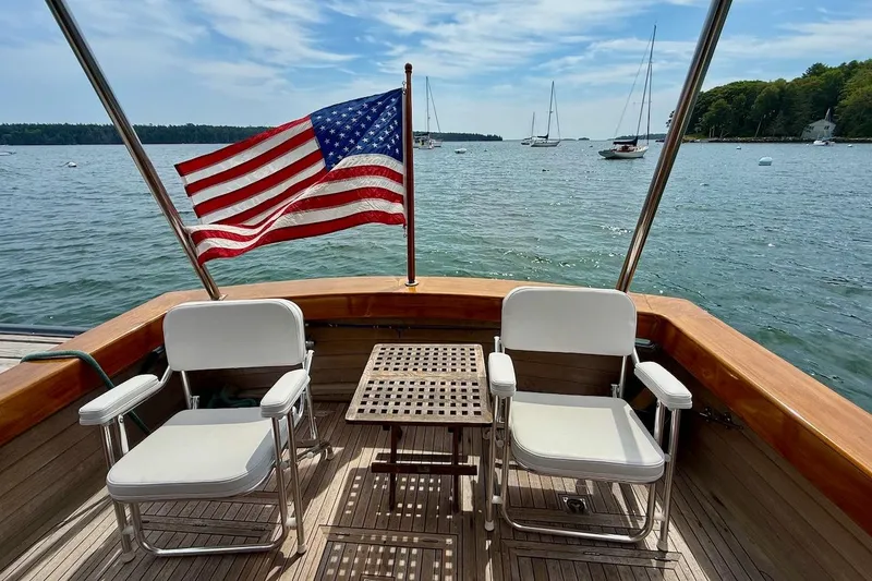 Slide: The Image of 1990 Nauset Flybridge Cruiser with American flag, chairs, and table on deck, overlooking serene waters. - 4