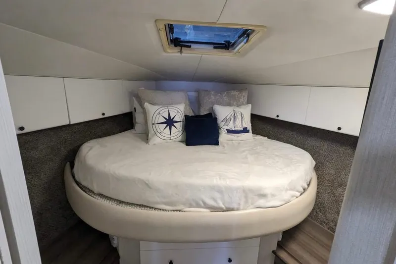 Slide: The Image of 1995 Silverton 34 Convertible cabin with round bed, nautical-themed pillows, and overhead hatch. - 21