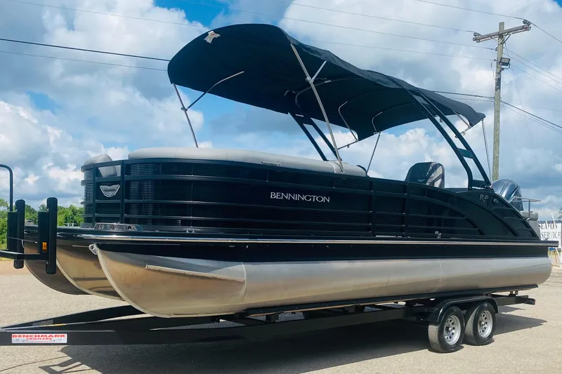 Slide: The Image of 2023 Bennington 25RSBA pontoon boat with black canopy on a trailer under a cloudy sky. - 11