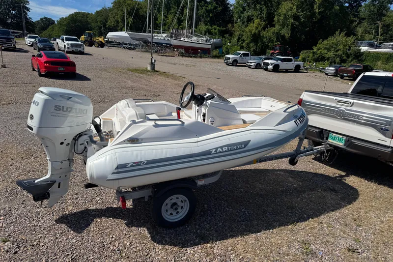 Slide: The Image of 2022 Zar Tender ZF0 boat on trailer, parked near vehicles, with Suzuki outboard motor. - 9