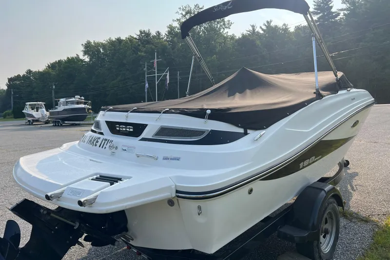 Slide: The Image of 2013 Sea Ray 190 Sport boat with cover, parked on a trailer in a lot. - 2