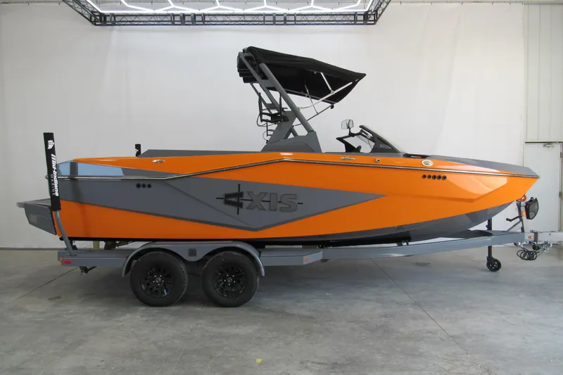 The Image of 2025 Axis T220 boat in vibrant orange and gray, displayed on a trailer indoors. - 1