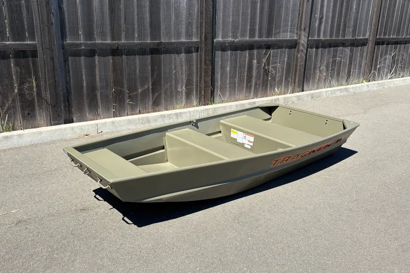 Slide: The Image of 2026 Tracker Grizzly 10 Jon boat on pavement, wooden fence background. - 2