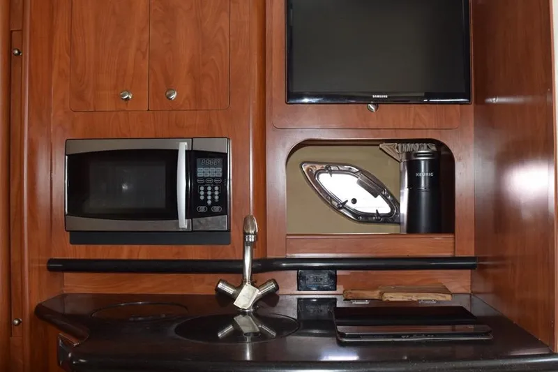 Slide: The Image of 2010 Rinker 310 Express Cruiser interior with microwave, sink, and TV in wooden cabinetry. - 29
