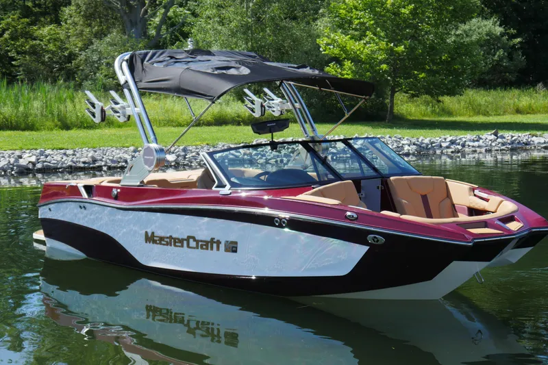 Slide: The Image of 2023 MasterCraft XT20 boat on calm water, surrounded by lush greenery. - 1