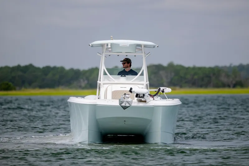 Slide: The Image of 2023 Twin Vee 240 GFX CC boat cruising on a calm lake with a person onboard. - 3