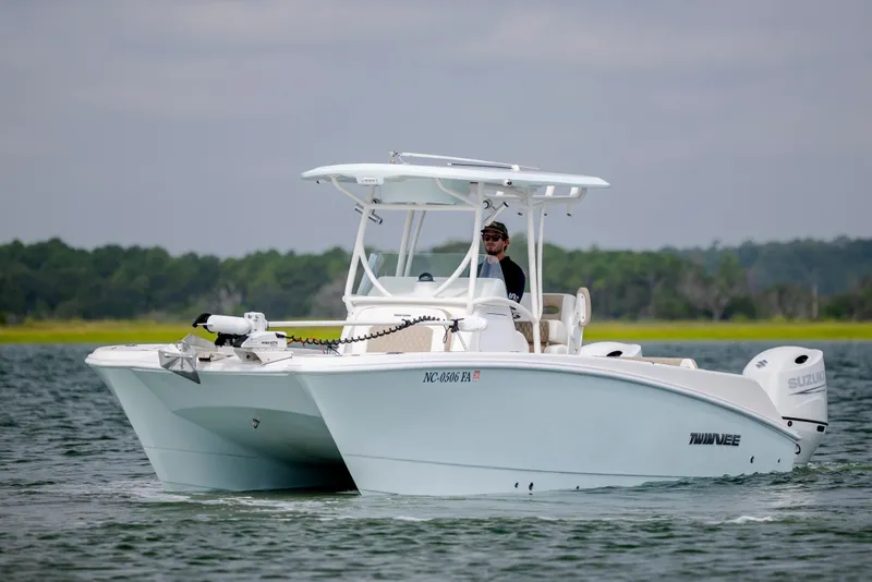 Slide: The Image of 2023 Twin Vee 240 GFX CC boat cruising on a calm lake with lush green background. - 4