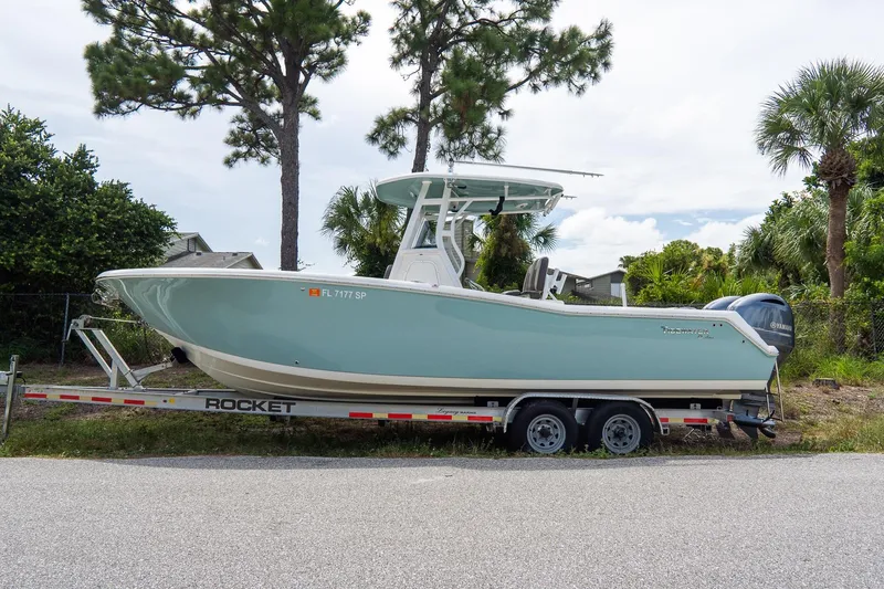 The Image of 2020 Tidewater 272 CC Adventure boat on trailer, parked near trees and greenery. - 1