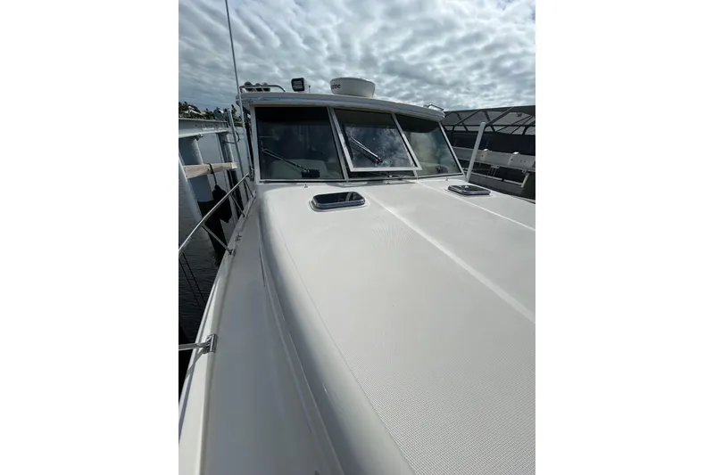 Slide: The Image of 2008 Mainship Pilot 34 boat with radar equipment, docked near waterfront homes under a cloudy sky. - 103