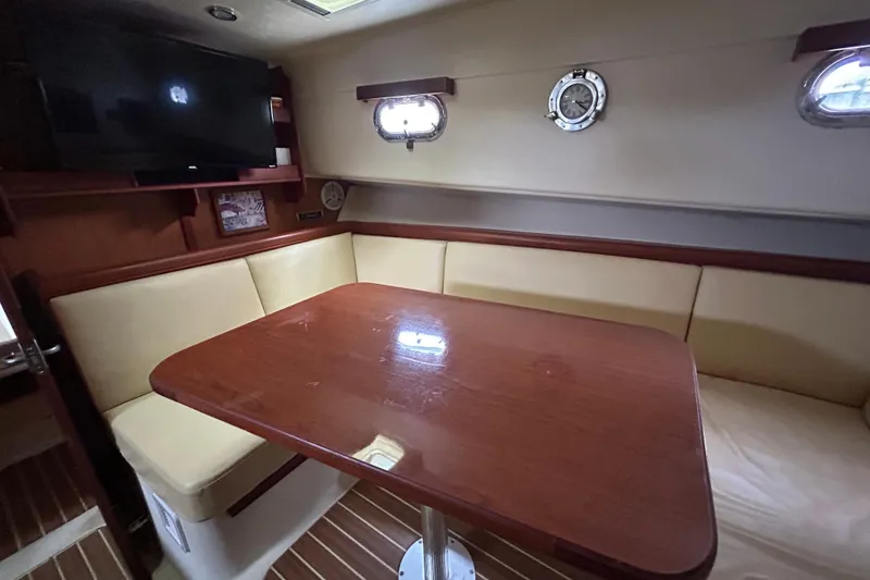 Slide: The Image of 2008 Mainship Pilot 34 interior with wooden table, beige seating, and mounted TV. - 44