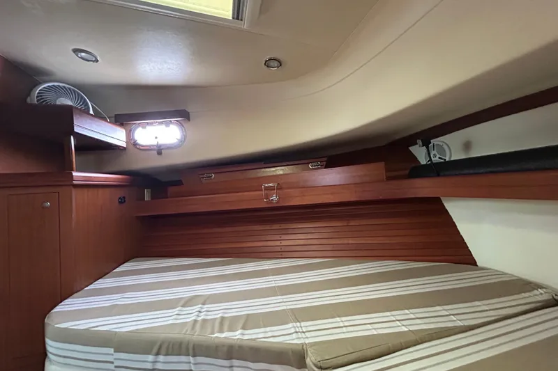 Slide: The Image of 2008 Mainship Pilot 34 cabin interior with striped bedding and wooden storage shelves. - 47