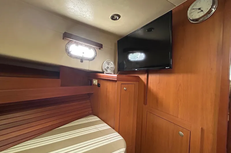 Slide: The Image of 2008 Mainship Pilot 34 cabin interior with TV, clock, and striped bedding. - 48