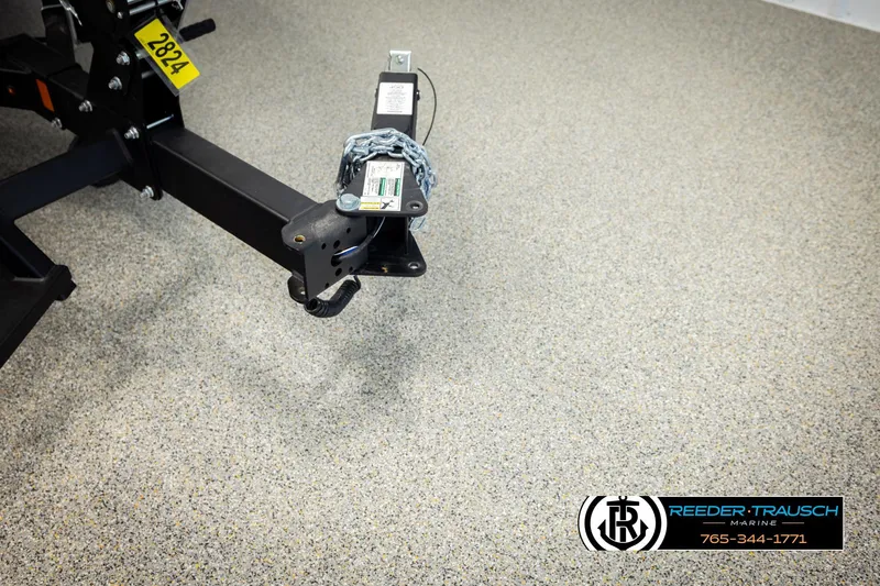 Slide: The Image of Trailer hitch of 2026 Lund 1875 Tyee boat on speckled floor, Reeder-Trausch Marine logo visible. - 47