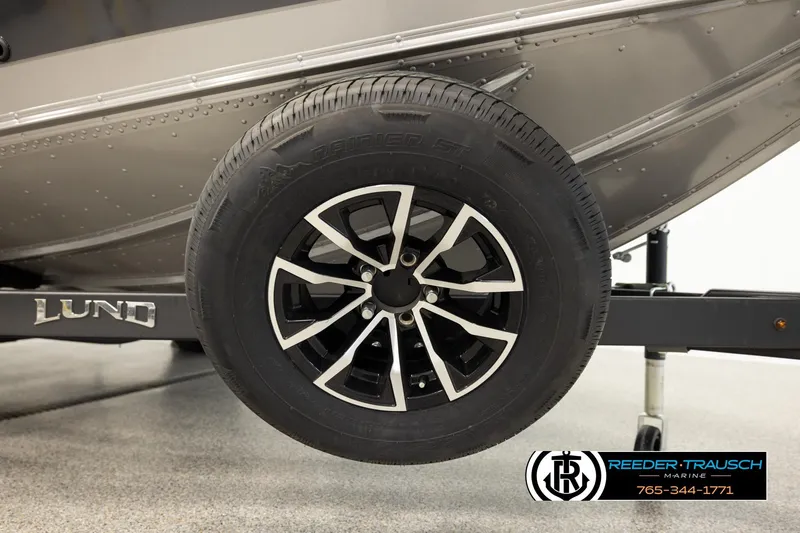 Slide: The Image of 2026 Lund 1875 Tyee boat trailer wheel, black alloy rim, Reeder-Trausch Marine logo. - 60